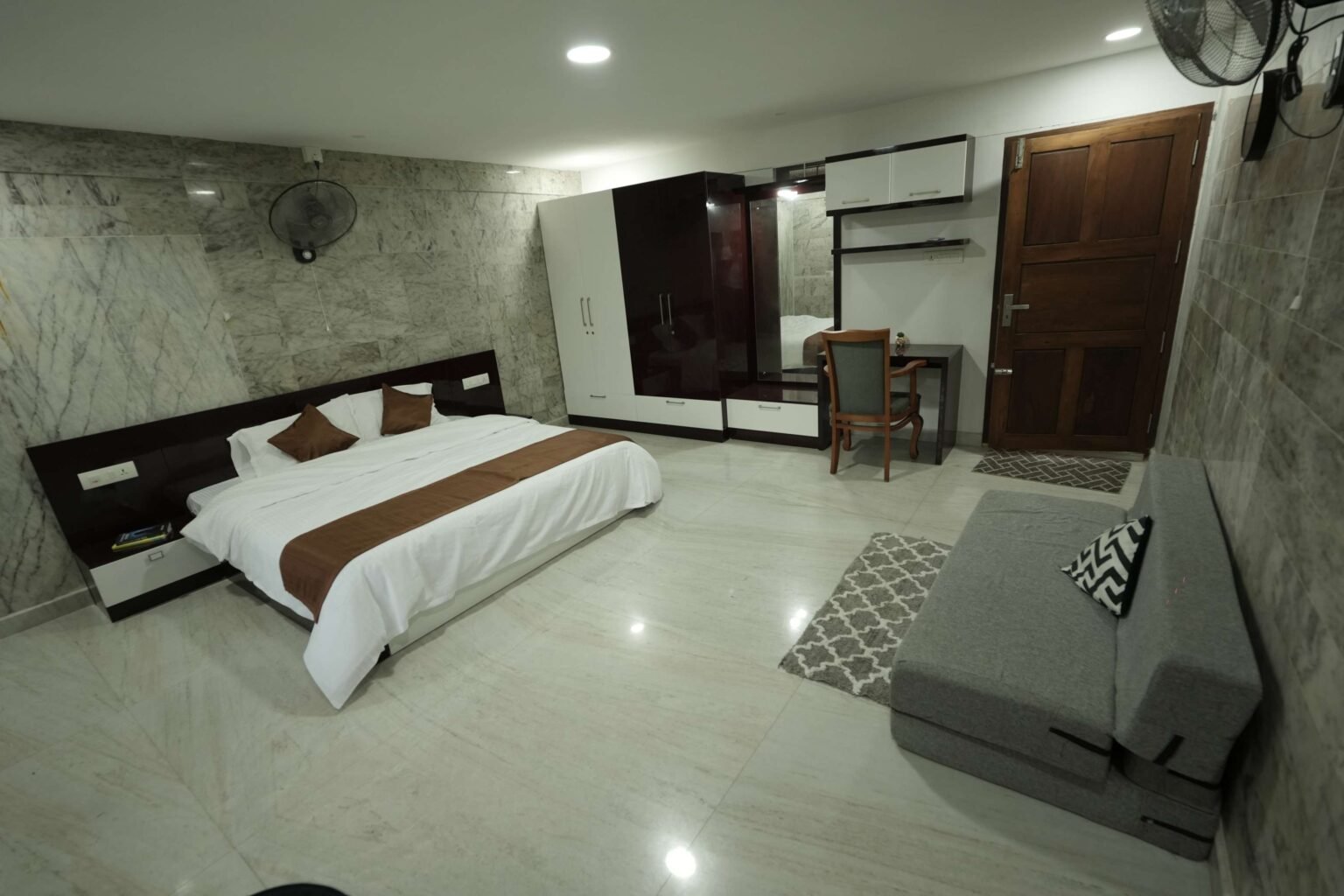 A bright bedroom with marble walls, a large double bed and a sofa