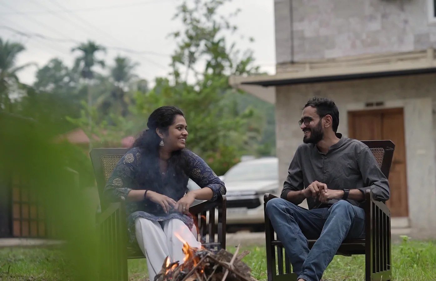 Two guests laughing beside a small bonfire in the garden